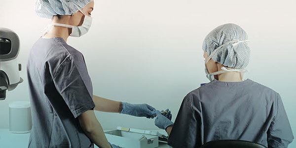 Assistentin reicht ein Instrument zur Vorbereitung der Haartransplantation